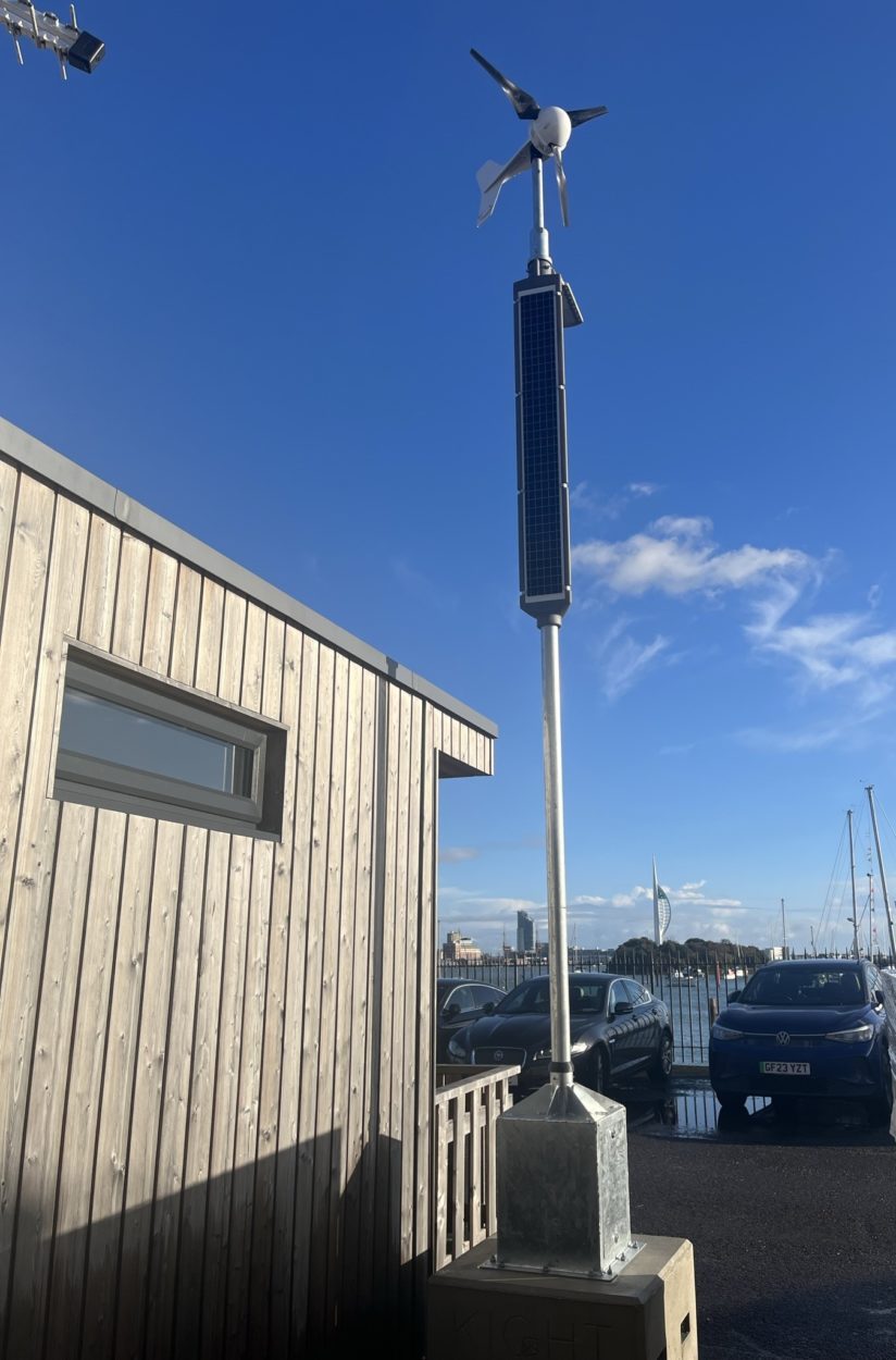 Lighting column with wind turbine and vertical solar panels placed next to office block