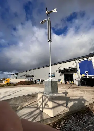 Off-grid portable site light with solar panels and wind turbine in parking area outside warehouse